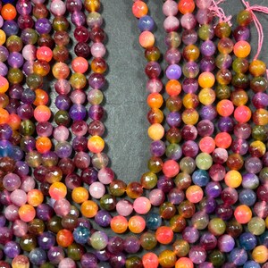 May include: A strand of faceted gemstone beads in shades of pink, purple, yellow, and orange. The beads are round and have a glossy finish.