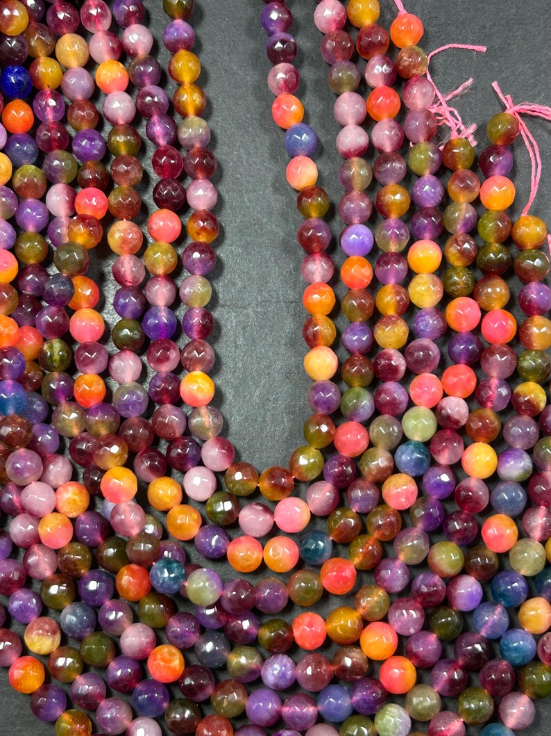 May include: A strand of faceted gemstone beads in shades of pink, purple, yellow, and orange. The beads are round and have a glossy finish.