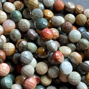 May include: A strand of multi-coloured gemstone beads with a faceted, rounded shape. The beads are a mix of brown, grey, green, and pink.