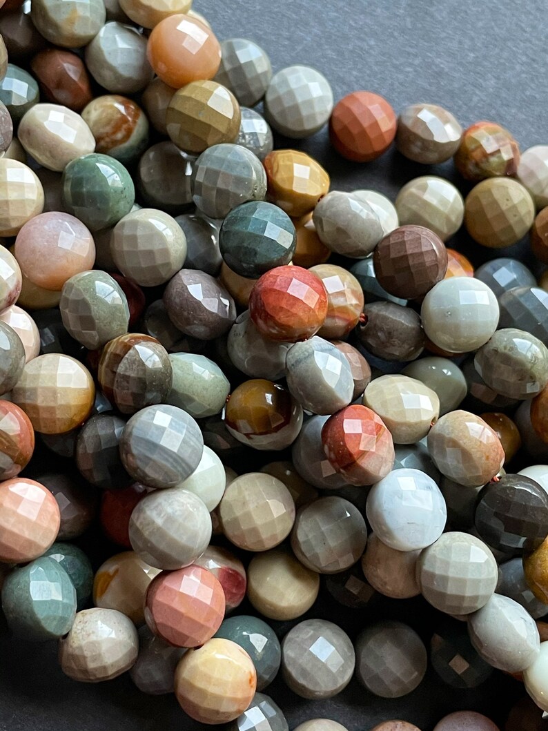 May include: A strand of multi-coloured gemstone beads with a faceted, rounded shape. The beads are a mix of brown, grey, green, and pink.
