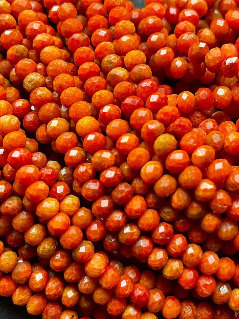 K&ouml;nnte beinhalten: Eine Str&auml;hne orangefarbener Korallenperlen mit einer facettierten, unregelm&auml;&szlig;igen Form. Die Perlen haben eine leuchtende orange Farbe mit einer leicht strukturierten Oberfl&auml;che.