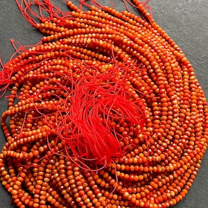 K&ouml;nnte beinhalten: Eine Str&auml;hne orangefarbener Karneolperlen, etwa 4 mm gro&szlig;, mit facettierter Oberfl&auml;che. Die Perlen sind auf rotem Faden aufgef&auml;delt und bereit f&uuml;r die Schmuckherstellung.