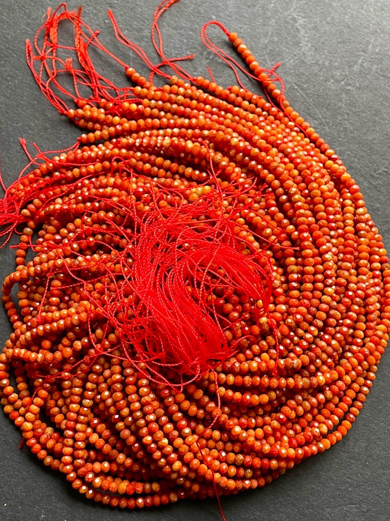 K&ouml;nnte beinhalten: Eine Str&auml;hne orangefarbener Karneolperlen, etwa 4 mm gro&szlig;, mit facettierter Oberfl&auml;che. Die Perlen sind auf rotem Faden aufgef&auml;delt und bereit f&uuml;r die Schmuckherstellung.
