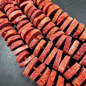 May include: Rows of red coral beads, each cut into a rectangular shape. The beads are strung together, creating a textured and organic appearance. The coral has a natural, porous surface and a deep red hue.