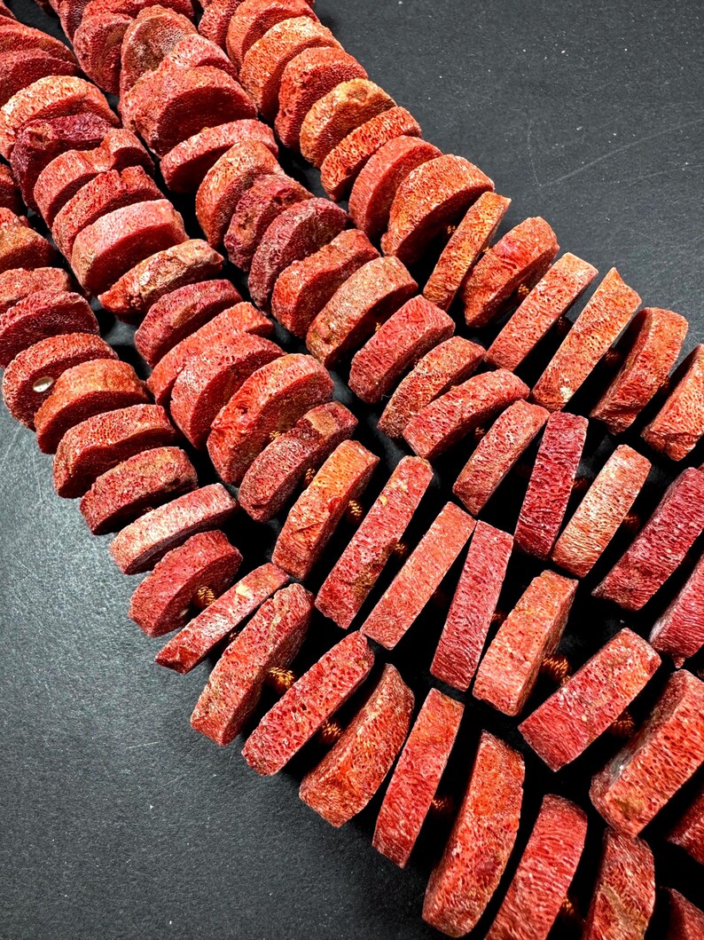 May include: Rows of red coral beads, each cut into a rectangular shape. The beads are strung together, creating a textured and organic appearance. The coral has a natural, porous surface and a deep red hue.