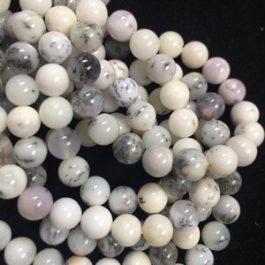 May include: A strand of white and gray dendritic opal beads. The beads are round and have a smooth, polished finish. The opal has a natural dendritic pattern, which gives it a unique and beautiful look.