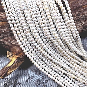 Op de afbeelding: Een streng witte zoetwaterparels, met een gladde, ronde vorm. De parels zijn aan elkaar geregen op een doorzichtige draad en ze zijn gerangschikt in een los, vloeiend patroon.