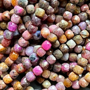 May include: Close-up of a collection of faceted gemstone beads in various shades of pink, brown, and orange. The beads are strung together on a red cord, creating a textured and colorful display. Ideal for jewelry making.