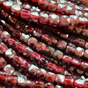 Może przedstawiać: Zbliżenie na sznur czerwonych koralików z kamieni szlachetnych. Koraliki są fasetowane i mają błyszczącą, odblaskową powierzchnię.