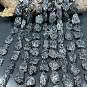 Puede incluir: Una hebra de cuentas de piedra natural negra, rugosa e irregular. Las cuentas son de forma y tamaño irregulares, con un brillo oscuro, casi metálico.