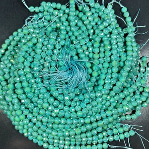 May include: A pile of teal green faceted beads with iridescent shimmer. The beads are strung on thin white thread.