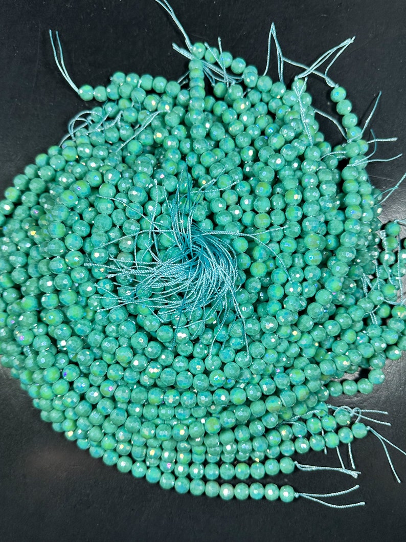 May include: A pile of teal green faceted beads with iridescent shimmer. The beads are strung on thin white thread.