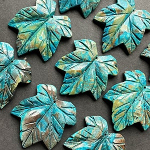 May include: A collection of eight teal and brown carved maple leaf pendants. The leaves are made of a marbled stone with a unique pattern.