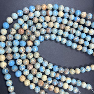 May include: A strand of blue, brown, and white jasper beads. The beads are round and have a speckled pattern. The beads are strung on a clear elastic cord.