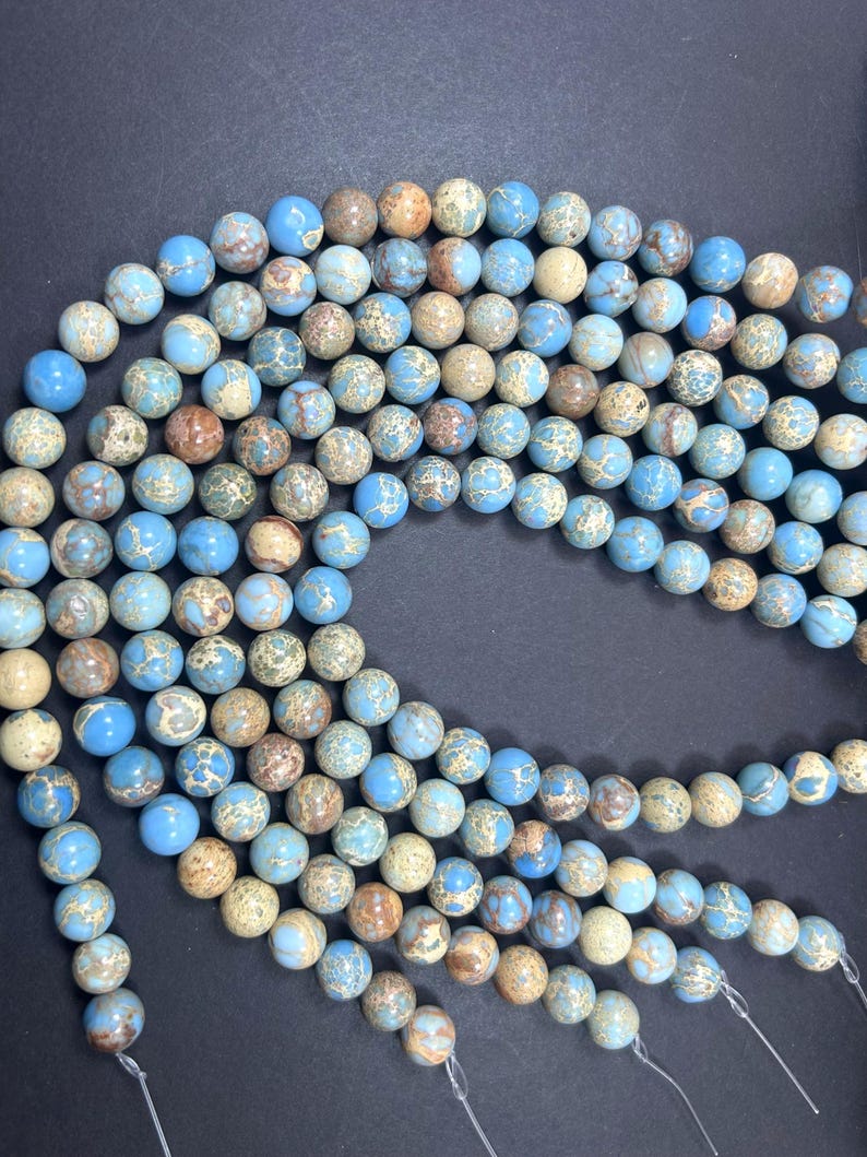 May include: A strand of blue, brown, and white jasper beads. The beads are round and have a speckled pattern. The beads are strung on a clear elastic cord.