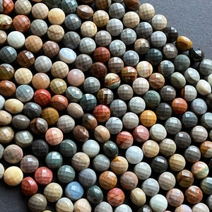May include: A strand of multi-coloured gemstone beads. The beads are faceted and have a round shape. The colours of the beads include brown, grey, red, and white.