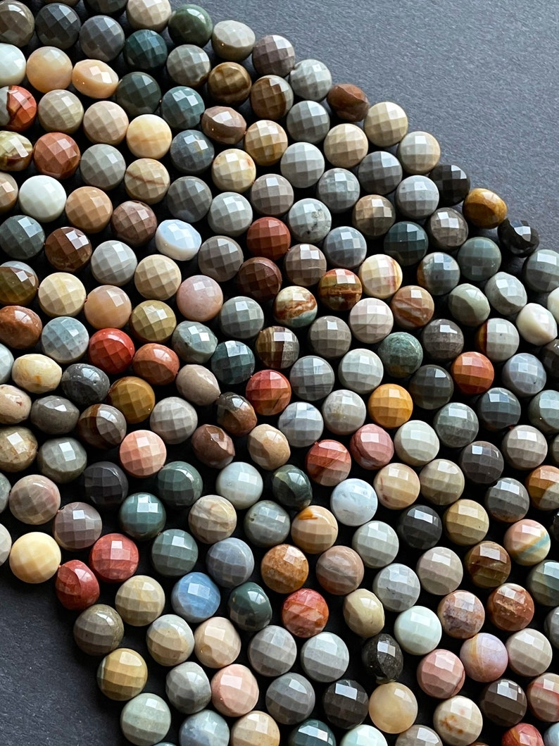 May include: A strand of multi-coloured gemstone beads. The beads are faceted and have a round shape. The colours of the beads include brown, grey, red, and white.