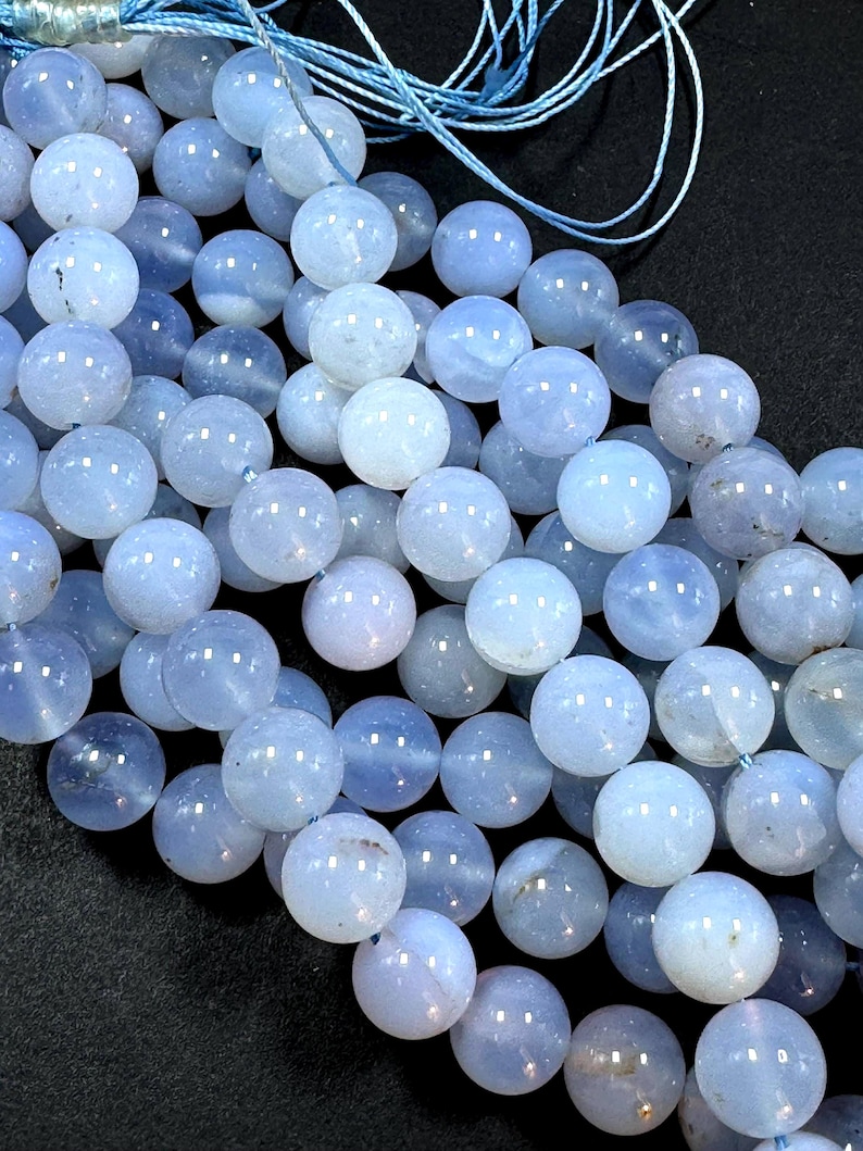 Pu&ograve; includere: Una collana di perle di agata blu chiaro, ogni perla &egrave; rotonda e liscia. Le perle sono infilate su un cordoncino blu sottile.