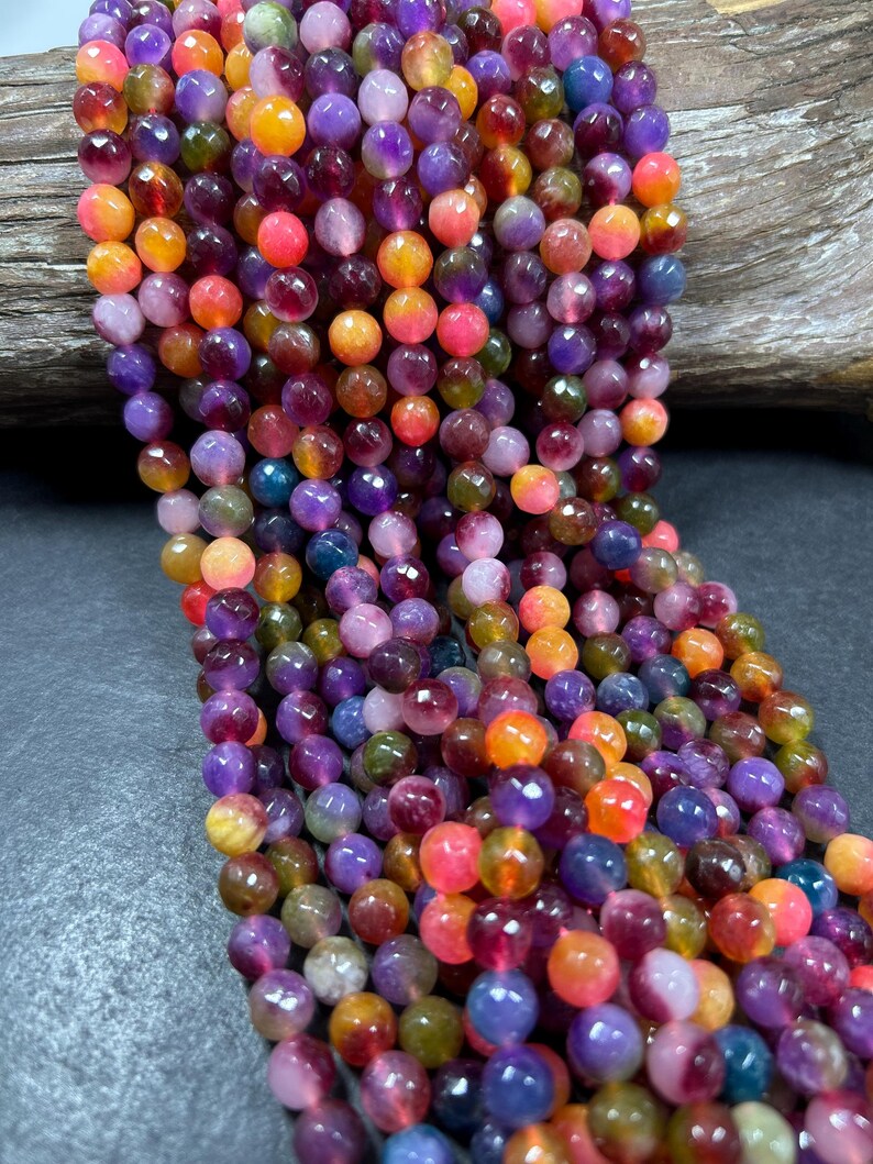 May include: A strand of colorful faceted gemstone beads. The beads are round and have a variety of colors, including purple, pink, orange, yellow, and green.