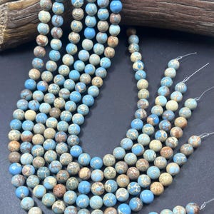 May include: A strand of blue and brown jasper beads. The beads are round and have a speckled pattern. The beads are strung on a clear elastic cord.