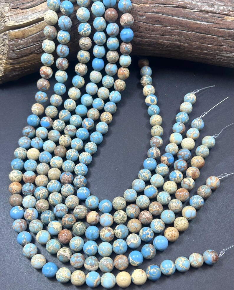 May include: A strand of blue and brown jasper beads. The beads are round and have a speckled pattern. The beads are strung on a clear elastic cord.