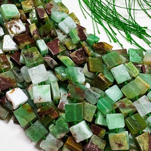 May include: A strand of green, brown, and white square-shaped gemstone beads. The beads are strung on green thread.