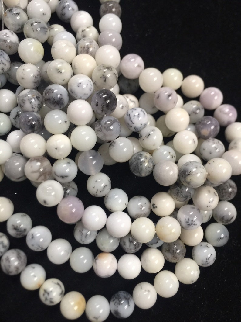 May include: A strand of white, gray, and black dendritic opal beads. The beads are round and smooth, and they have a natural, organic look.