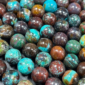 Puede incluir: Primer plano de una colección de cuentas redondas, lisas, de color turquesa y marrón. Las cuentas tienen un aspecto moteado y veteado con tonos de verde, azul, marrón y negro.