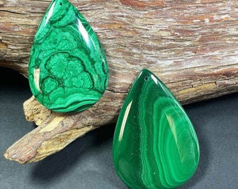 May include: Two green malachite gemstone pendants in the shape of teardrops. The pendants have a smooth, polished finish and intricate patterns.