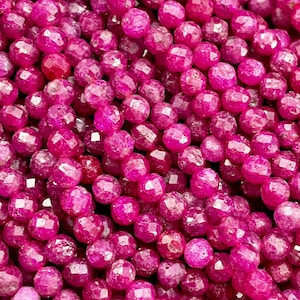 May include: A close-up of a strand of pink faceted gemstone beads. The beads are round and have a smooth, polished finish.