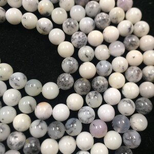 May include: A strand of white and gray dendritic opal beads. The beads are round and have a smooth, polished finish.