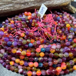 May include: A strand of multi-colored faceted gemstone beads. The beads are a mix of purple, pink, orange, and yellow. The beads are strung on a pink thread.