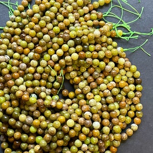 May include: A strand of green and brown gemstone beads. The beads are round and have a natural, polished finish. The beads are strung on a thin, green thread.