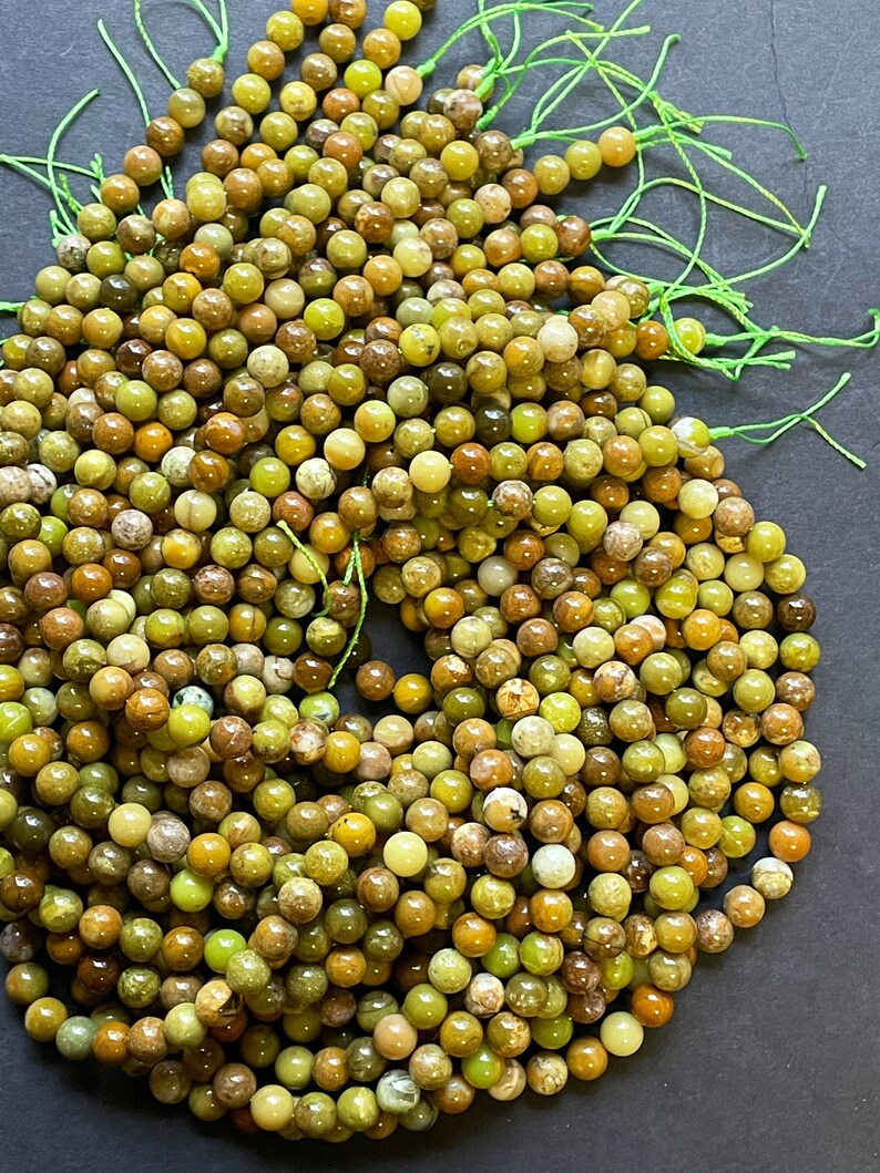 May include: A strand of green and brown gemstone beads. The beads are round and have a natural, polished finish. The beads are strung on a thin, green thread.