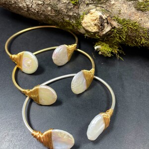 Pu&ograve; includere: Tre braccialetti avvolti in filo d'oro e d'argento con accenti di perle bianche. Ogni braccialetto presenta una forma e una dimensione di perla diverse.