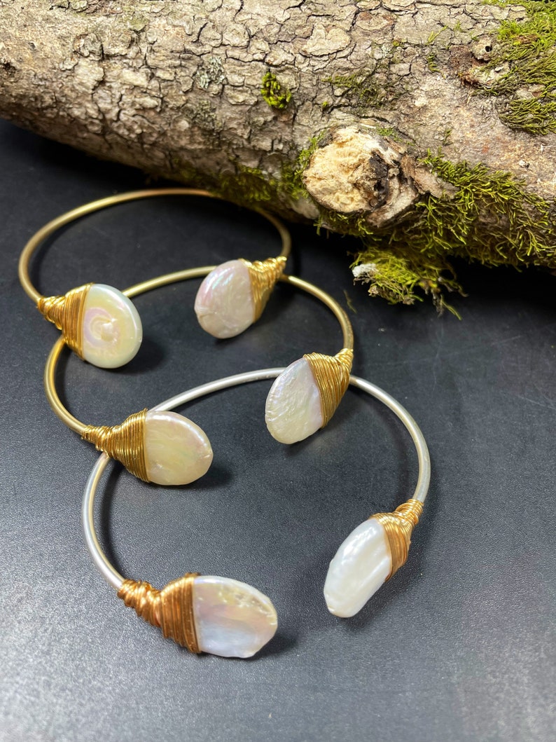 Pu&ograve; includere: Tre braccialetti avvolti in filo d'oro e d'argento con accenti di perle bianche. Ogni braccialetto presenta una forma e una dimensione di perla diverse.