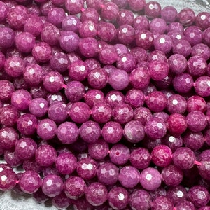 May include: Close-up of a strand of faceted, round beads in a deep magenta color. The beads are strung together on a pink string, creating a textured surface. These beads are suitable for jewelry making.