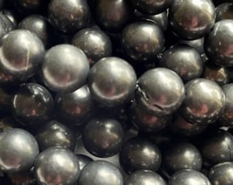 May include: A close-up of a pile of black pearl beads. The beads are round and smooth, with a high-gloss finish.