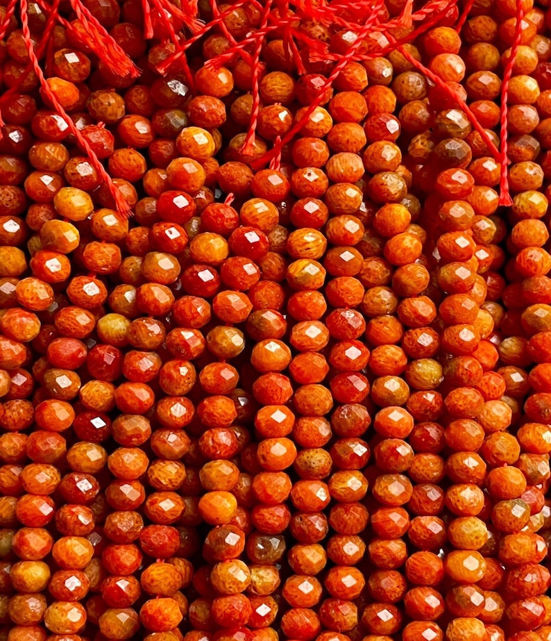K&ouml;nnte beinhalten: Eine Str&auml;hne orangefarbener Korallenperlen, jede Perle ist facettiert und hat eine raue, strukturierte Oberfl&auml;che.