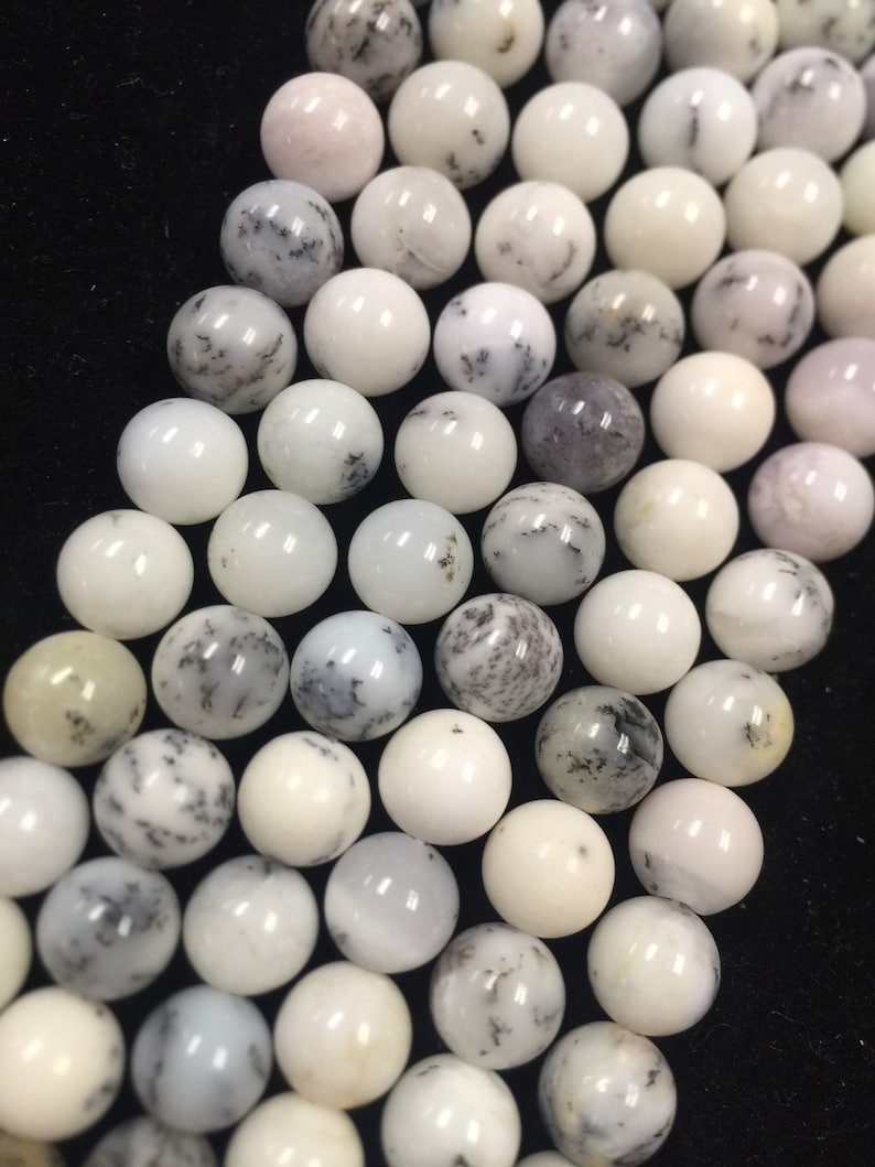 May include: A strand of white and gray dendritic opal beads. The beads are round and have a smooth, polished finish.
