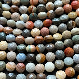 May include: A strand of faceted gemstone beads in various shades of brown, grey, red, and blue. The beads are round and have a polished, faceted surface.