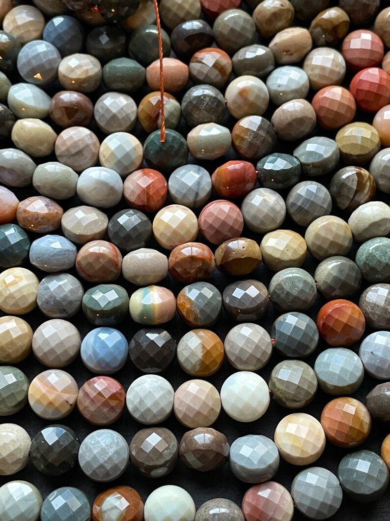 May include: A strand of faceted gemstone beads in various shades of brown, grey, red, and blue. The beads are round and have a polished, faceted surface.
