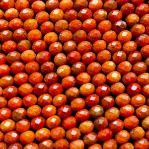 K&ouml;nnte beinhalten: Nahaufnahme einer Kette aus orangefarbenen Korallenperlen. Die Perlen sind facettiert und haben ein nat&uuml;rliches, organisches Aussehen.