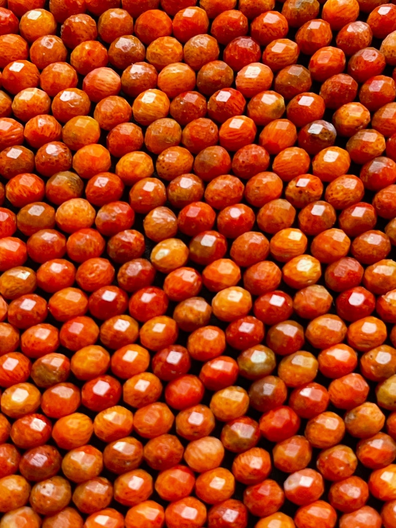 K&ouml;nnte beinhalten: Nahaufnahme einer Kette aus orangefarbenen Korallenperlen. Die Perlen sind facettiert und haben ein nat&uuml;rliches, organisches Aussehen.
