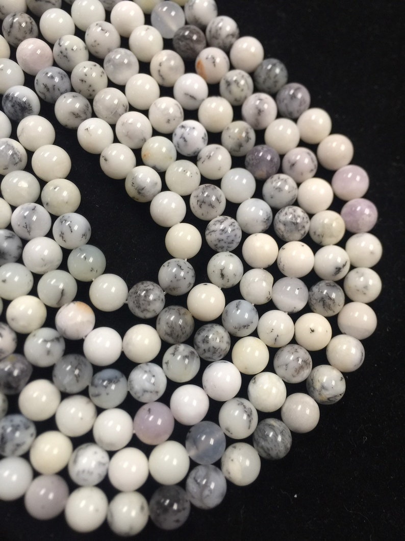 May include: A strand of white and gray dendritic opal beads. The beads are round and have a smooth, polished finish.