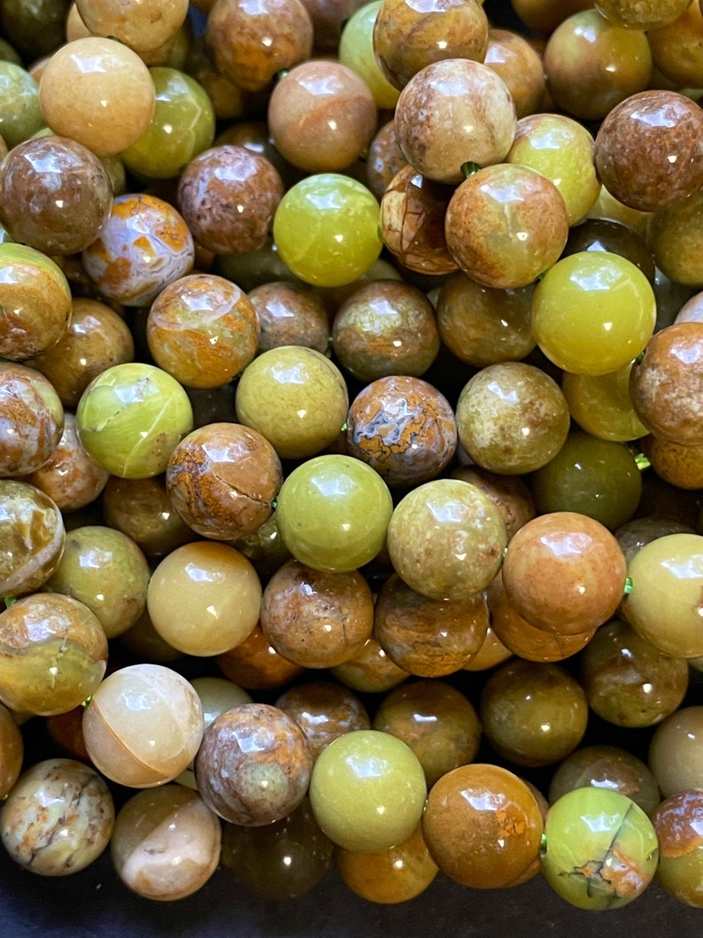 May include: A strand of green and brown opal beads. The beads are round and have a smooth, polished finish. They are perfect for making jewelry.
