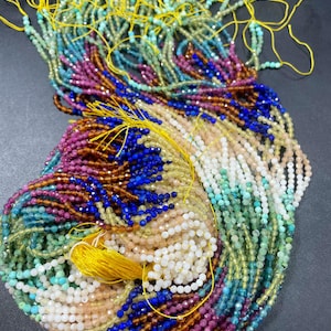 May include: A collection of colourful gemstone bead strands, including turquoise, blue, green, yellow, pink, and white. The strands are tied together with yellow thread.