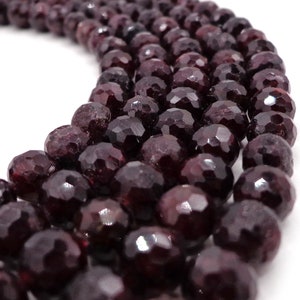 May include: A strand of dark red faceted gemstone beads. The beads are round and have a smooth, polished finish.
