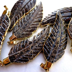 May include: A set of six gold-toned leaf-shaped pendants with a dark gray fossilized stone inlay. The pendants are approximately 2 inches long and have a loop at the top for attaching to a chain or cord.