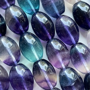May include: A strand of oval-shaped fluorite beads with a gradient of purple, blue, and green colors. The beads are smooth and polished, with a glossy finish.